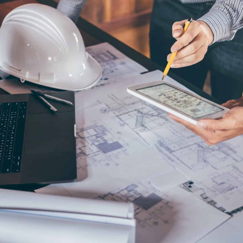 Construction engineering or architect discussing a blueprint and building model while checking information on sketching meeting for architectural project in work site.